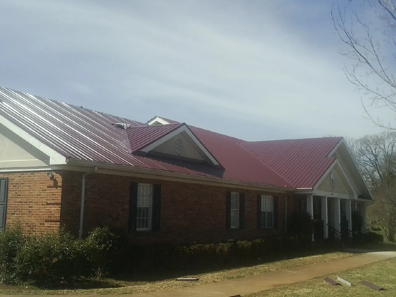 Red metal roof with gabled entries on a long brick building, from a Hail Damage Roof Repair job in Nucla