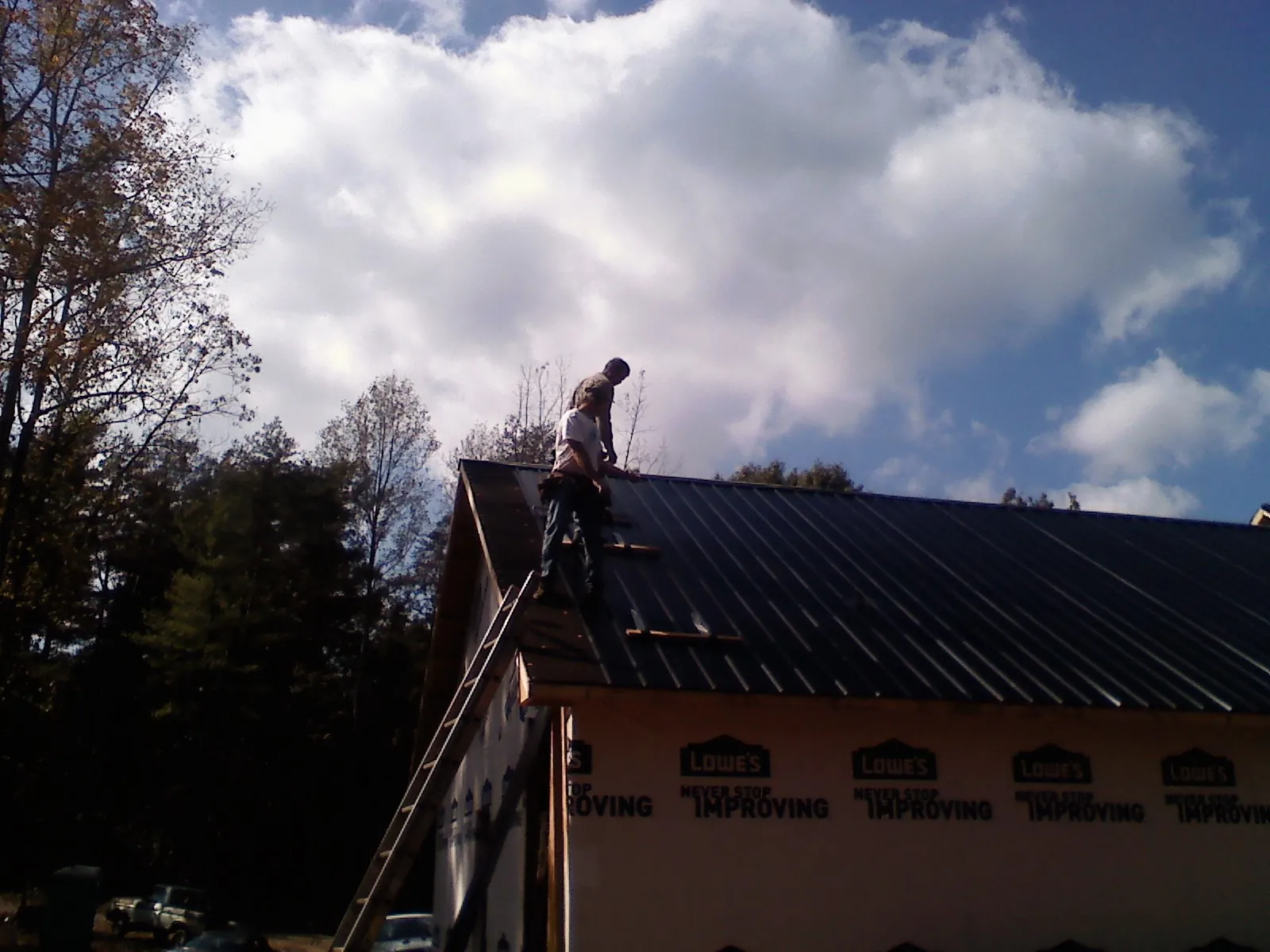 Roofer fastening dark metal panels high against a cloudy sky, from a Roof Inspection job in Nucla