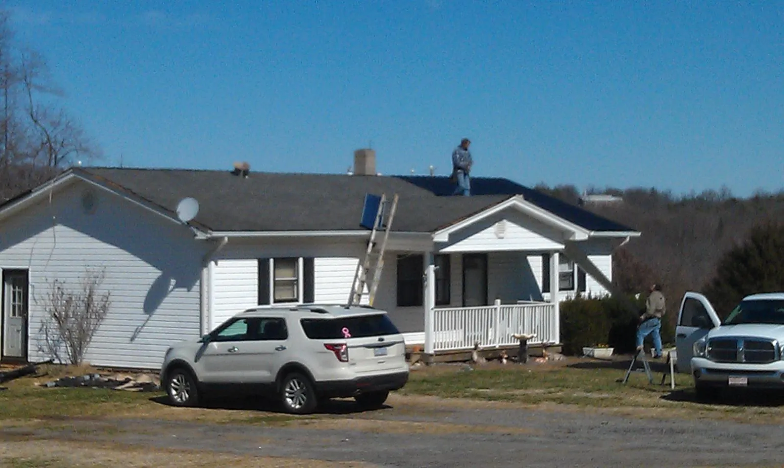 Roofers stripping shingles from a white ranch house roof in Nucla